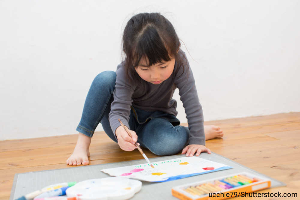 床に座って、クレヨンと絵の具でお絵描きしている女の子