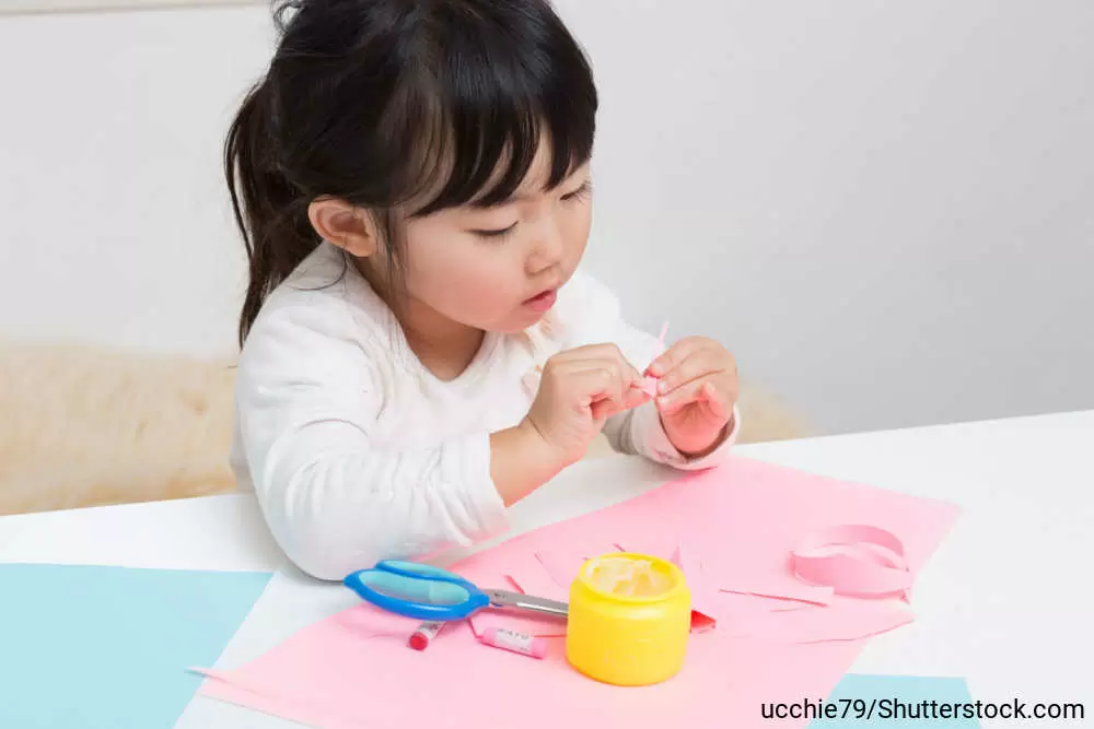 つぼに入ったのりやハサミを使って、色紙で工作している女の子