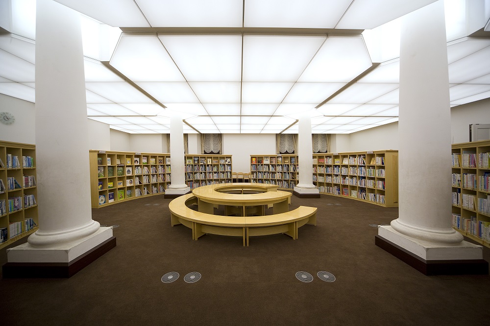 中央に大きな円形テーブルと、その周りを囲む本棚、太い柱のある「子どものへや」