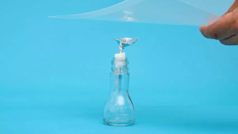 アルミホイルとガラス瓶で作った静電気探知機にクリアファイルを近づけているところ