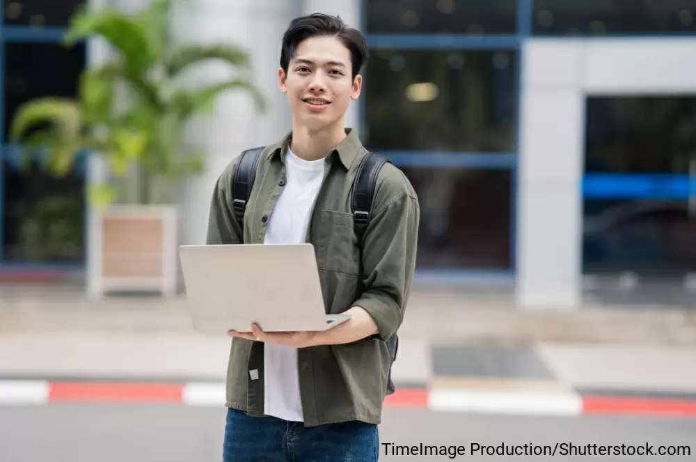 ノートパソコンを手にする大学生風の若い男性