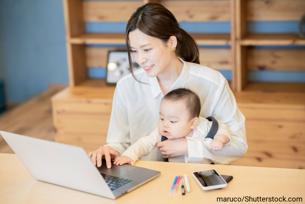 赤ちゃんを抱っこしてノートパソコンで作業する母親