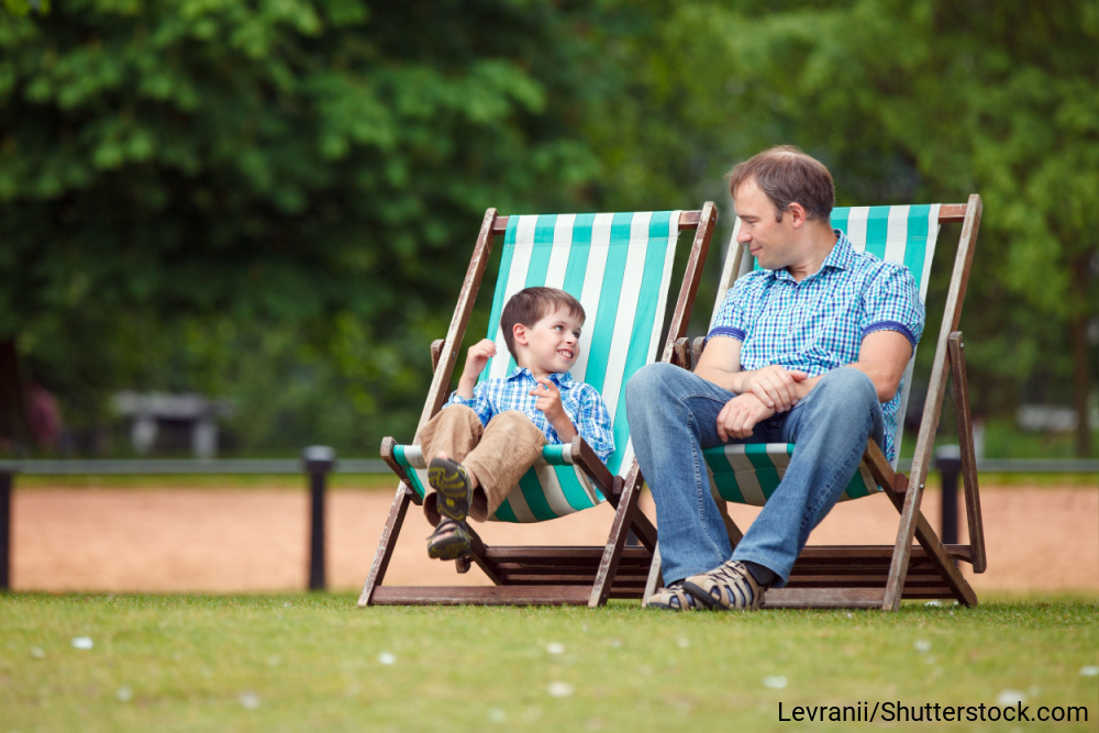 公園の椅子に座って微笑み合う、イギリス人の父と息子