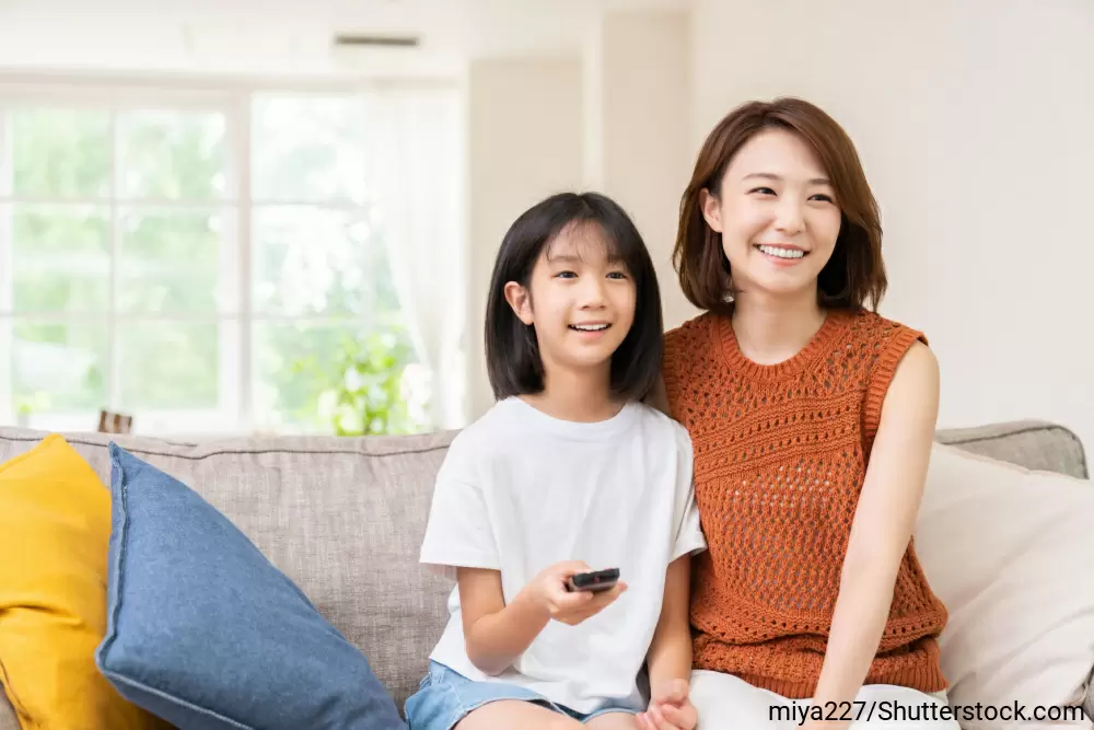 ソファに座って並んでテレビを見ている母と娘