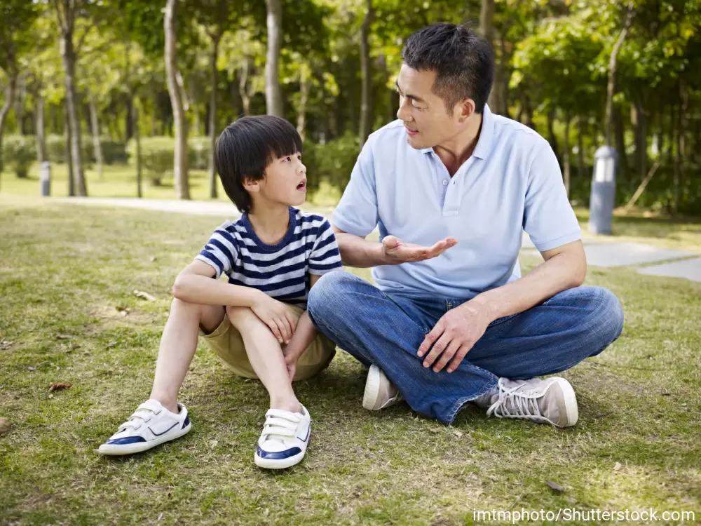 芝生の上に座って男の子の話を聞いているお父さん