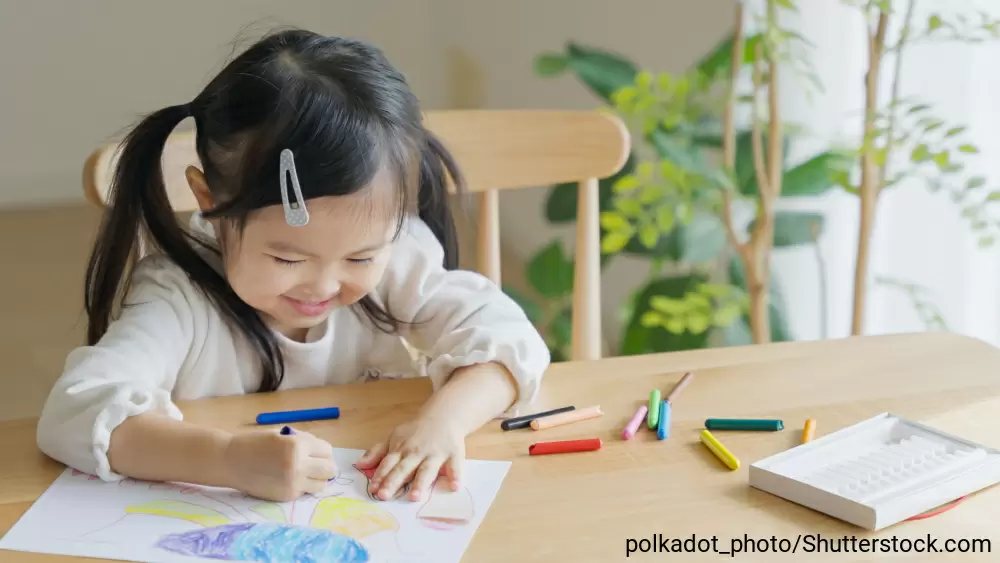 テーブルの上でクレヨンでお絵描きをしている女の子
