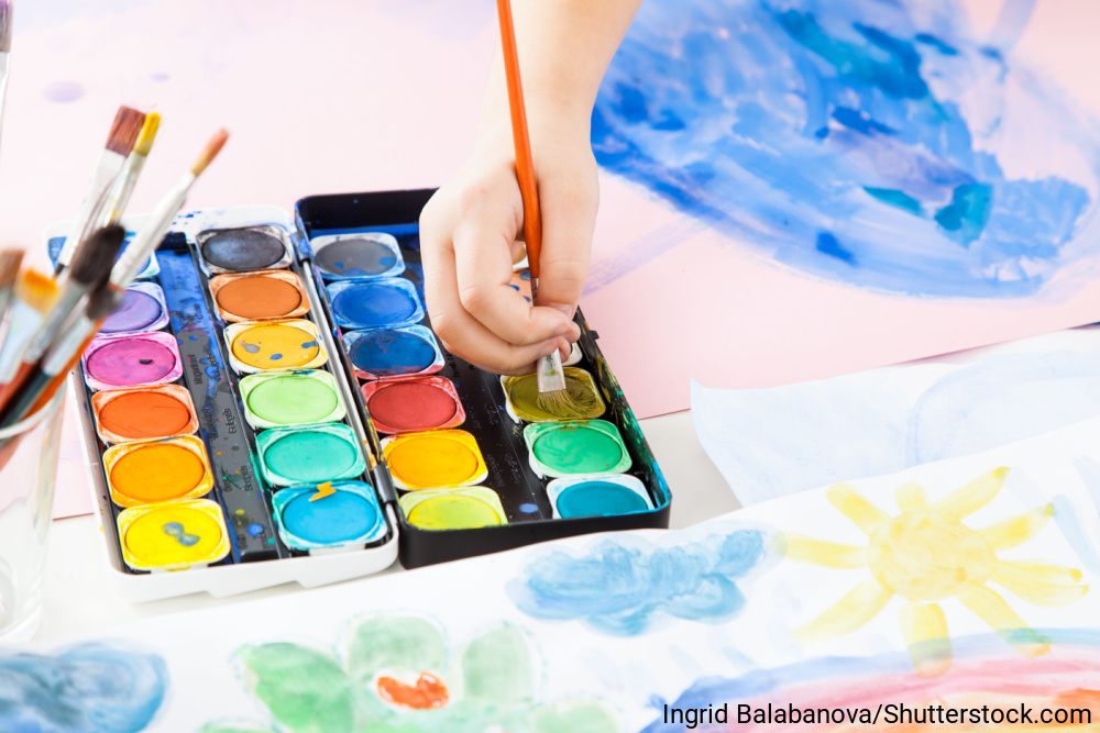 絵筆を握る子どもの手とパレット、絵の具で描かれた水彩の絵