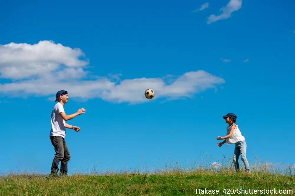 芝生の上でサッカーボールを投げて遊んでいるお父さんと娘