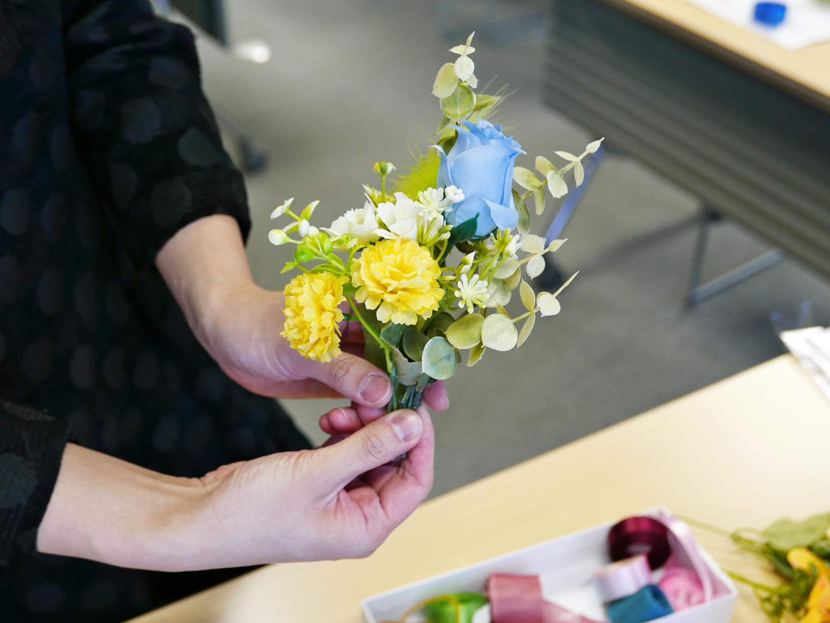 水色、黄色、白色の花でできたコサージュを手にする人