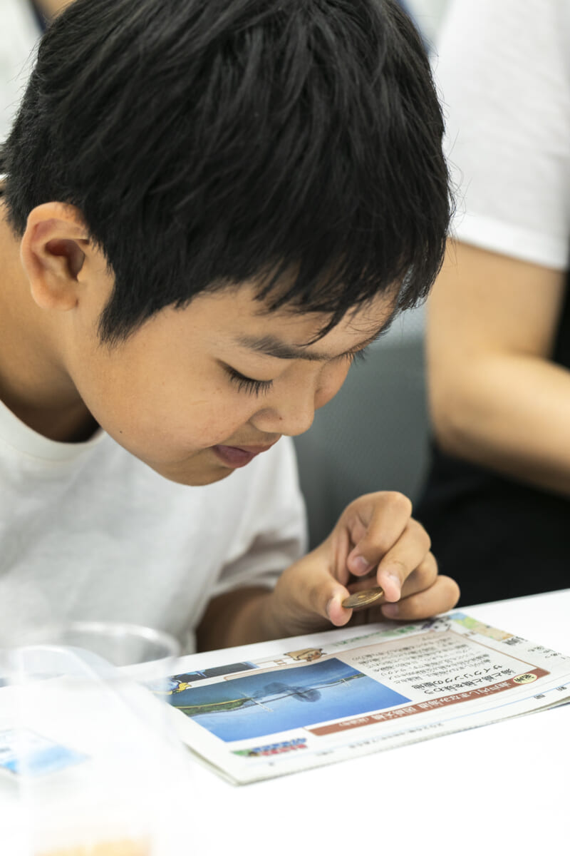 5円玉レンズ越しに新聞紙を読む男の子